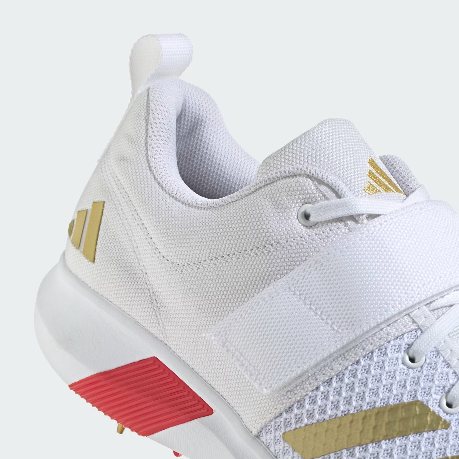 White athletic shoe with gold accents and a red sole on a white background